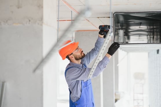 Hombre con casco de seguridad utilizando taladro sobre ducto de metal